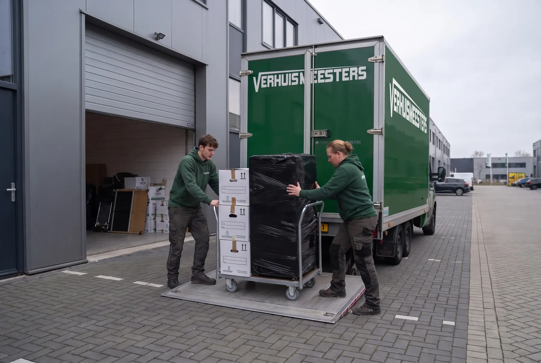 Verhuizers van VerhuisMeesters rijden een rolcontainer met verhuisdozen de laadklep op bij een bedrijfspand